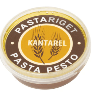 Klar plastbøtte med låg, brun-gul etiket, "Pastariget Kantarel Pasta Pesto" med hvedeillustration.