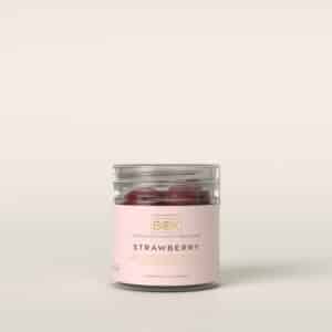 Klar beholder med lyserødt mærkat, der viser røde, runde slik. Teksten "STRAWBERRY" er synlig.