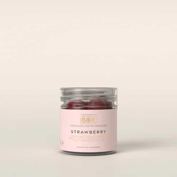 Klar beholder med lyserødt mærkat, der viser røde, runde slik. Teksten "STRAWBERRY" er synlig.